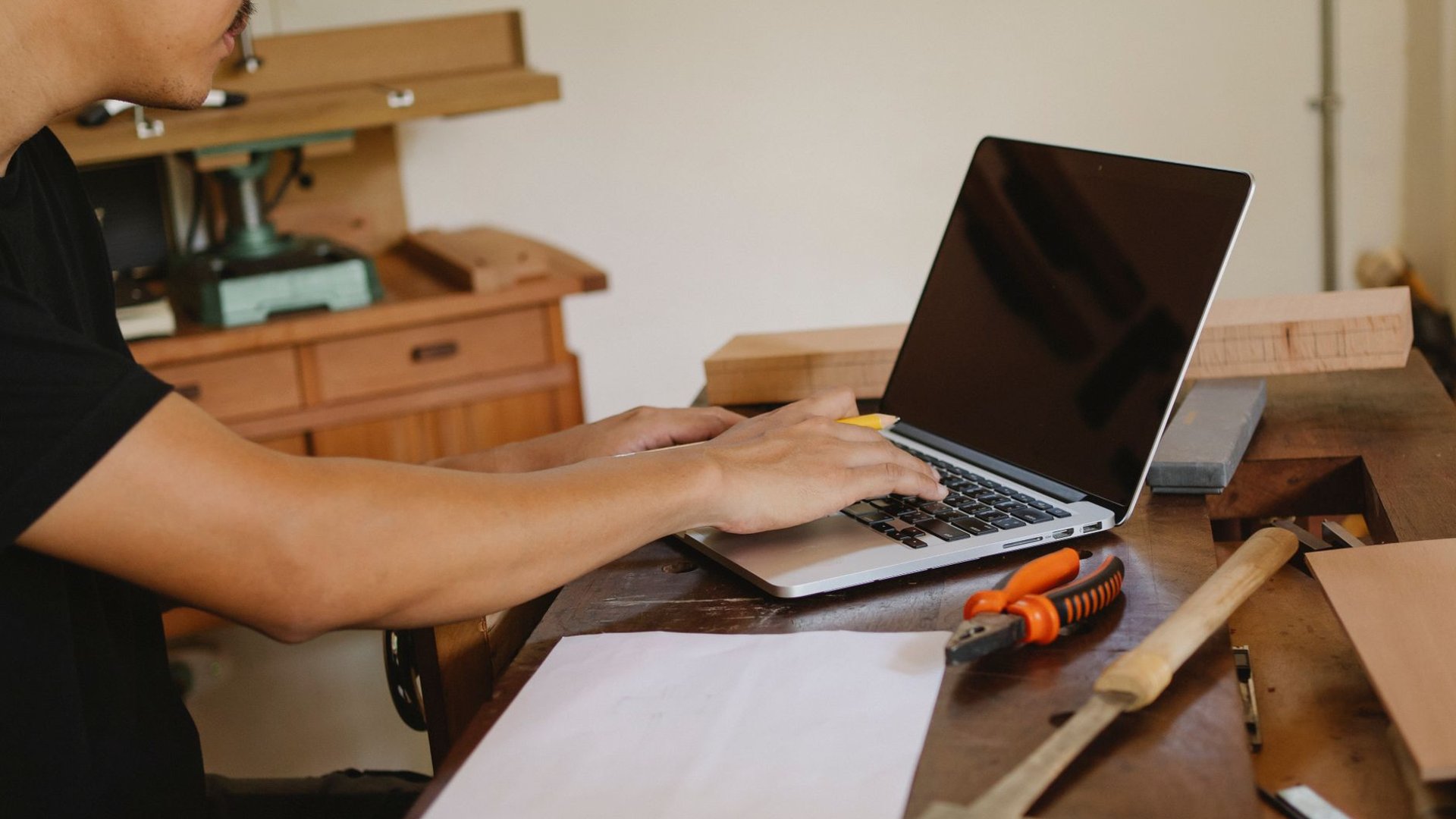 Handwerker schreibt eine Rechnung am Laptop auf der Werkbank